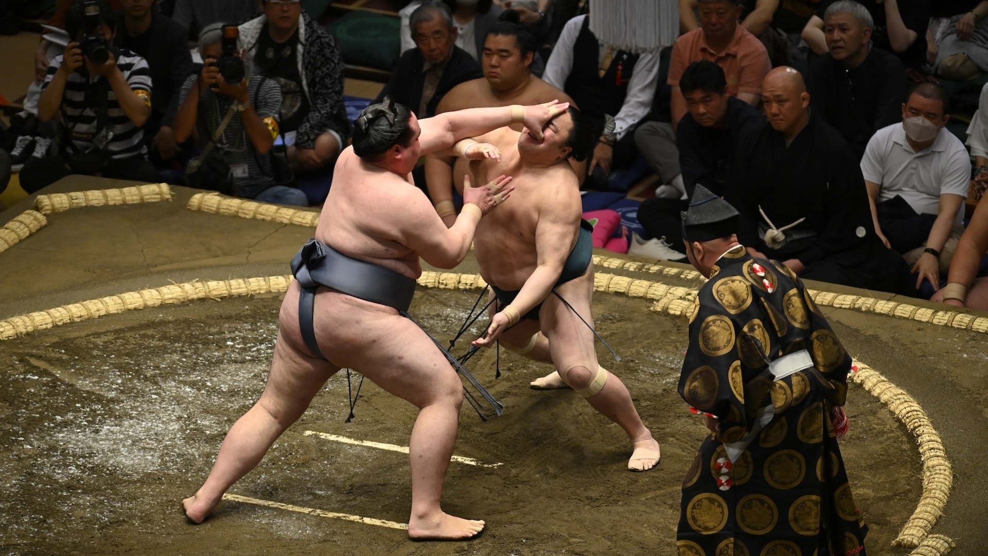 Two sumos competing with a ref stood beside them 