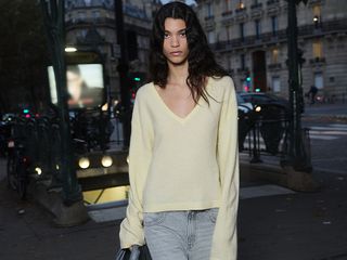 Model wears butter yellow v-neck sweater and jeans while walking at night.