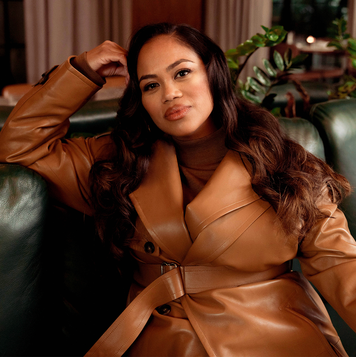 Zinzi Coogler wearing a camel leather jacket on a leather sofa