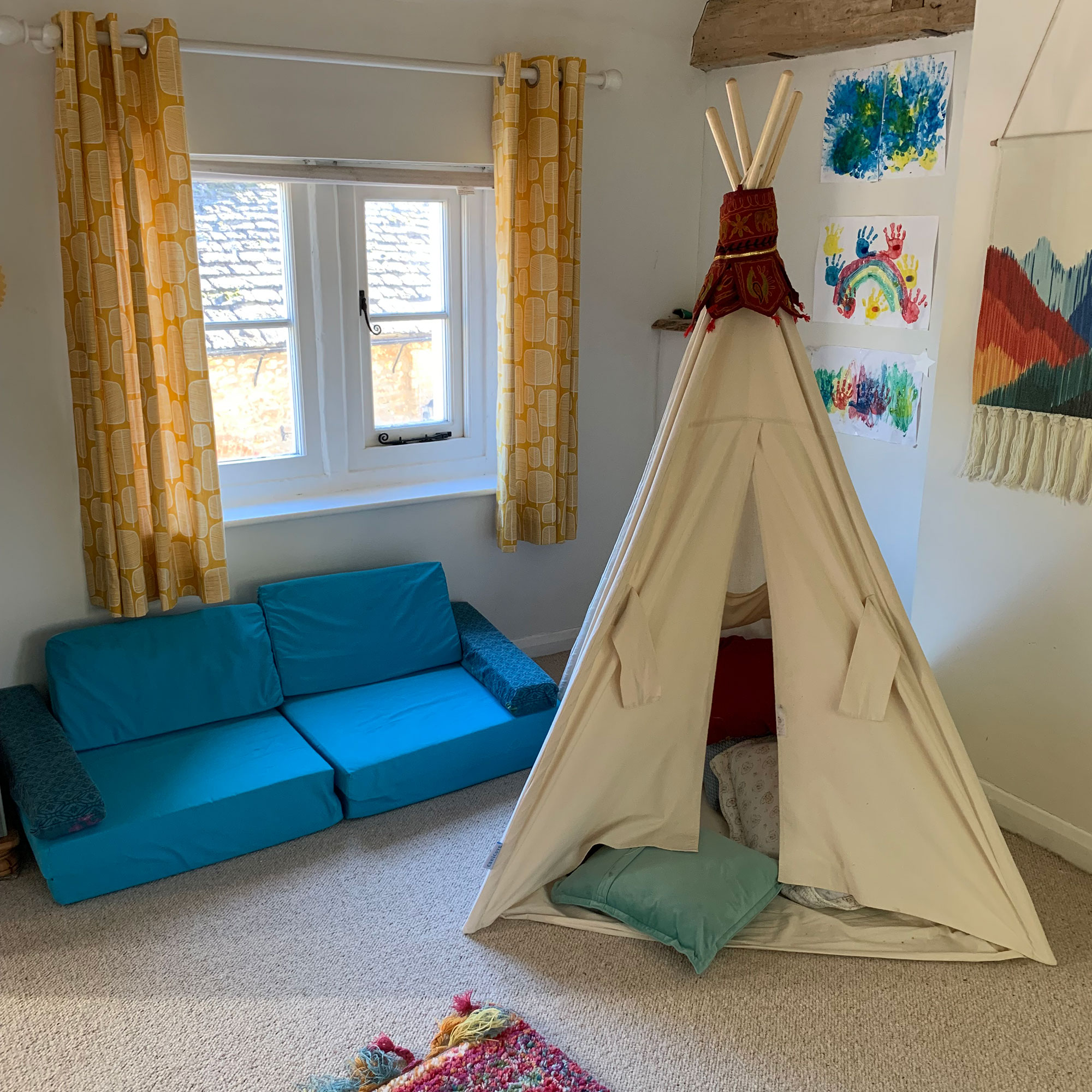 Child's play room with teepee style tent in front of wall covered with colourful artwork