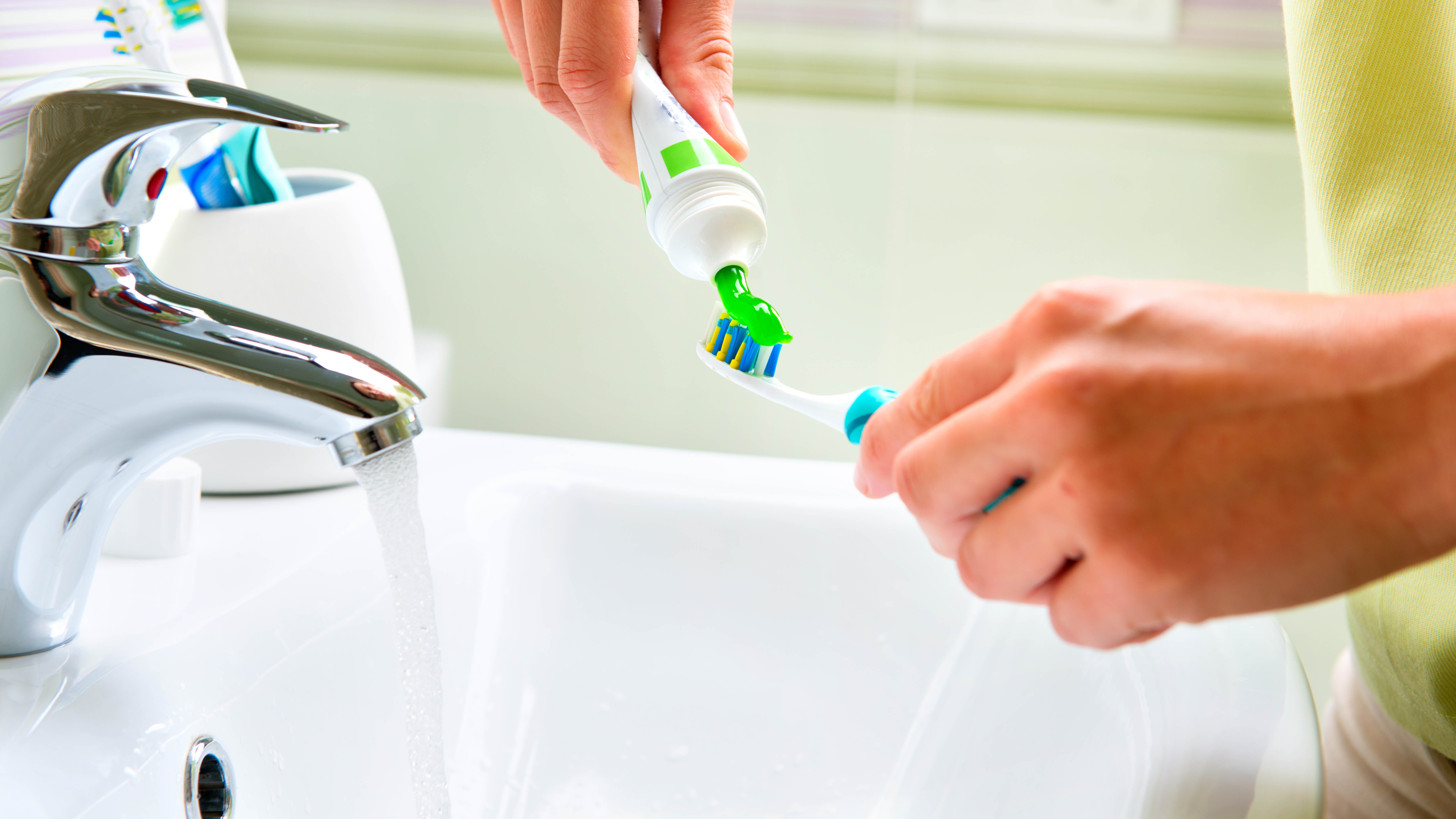 Toothpaste being applied to a toothbrush while the tap is running