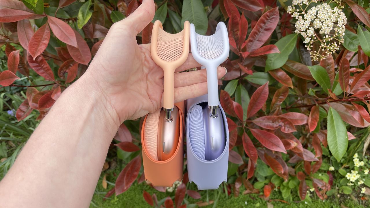Apple AirPods Max 2 in orange with AirPods Max just visible in purple, outside in a garden on a bench, held in a hand