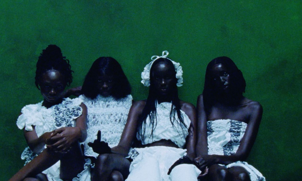 Photo of four young Black women against a green wall, by photographer Gabriel Moses