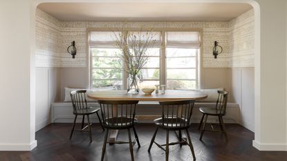 main neutral dining area with oval wooden table, dark Windsor chairs and patterned wallpaper 