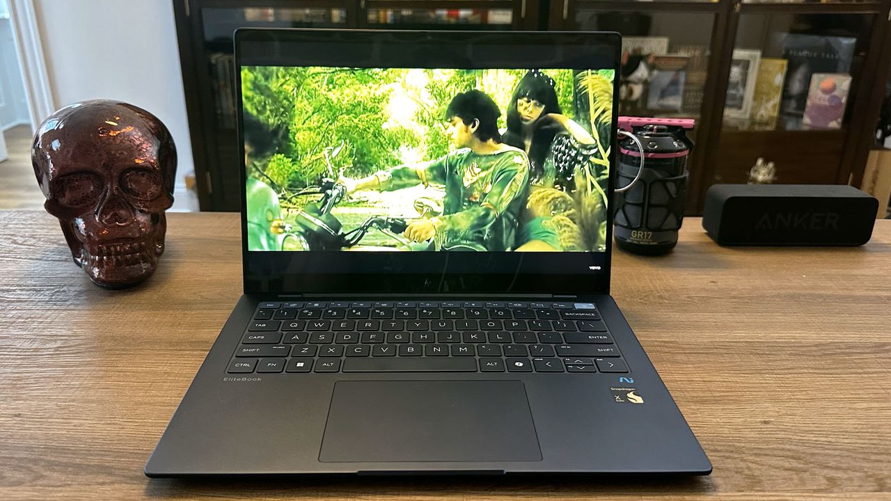 An open and powered on laptop on top of a wooden desk, showing a scene from a movie on its screen.