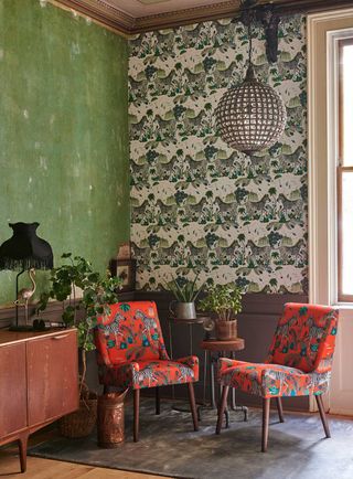 Living room with green walls and a feature wall with a zebra motif print,. Two red armchairs sit in front of the wall.