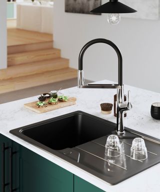 A striking black kitchen sink with a modern chrome and black spring neck tap. A marble worktop and deep green cabinetry add contrast to the stylish design.