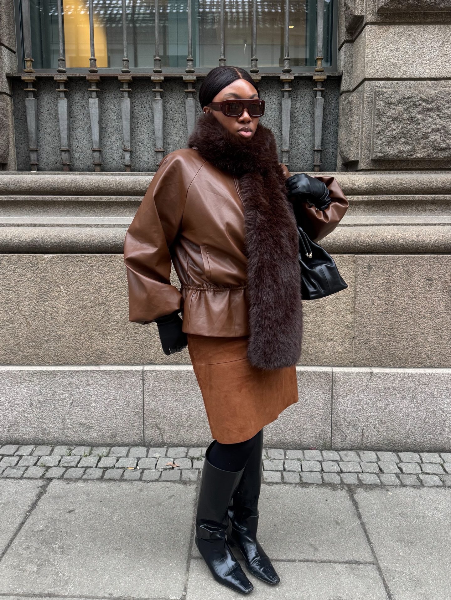 An image of @nnennaechem wearing a fur stole with a suede skirt and knee-high boots.