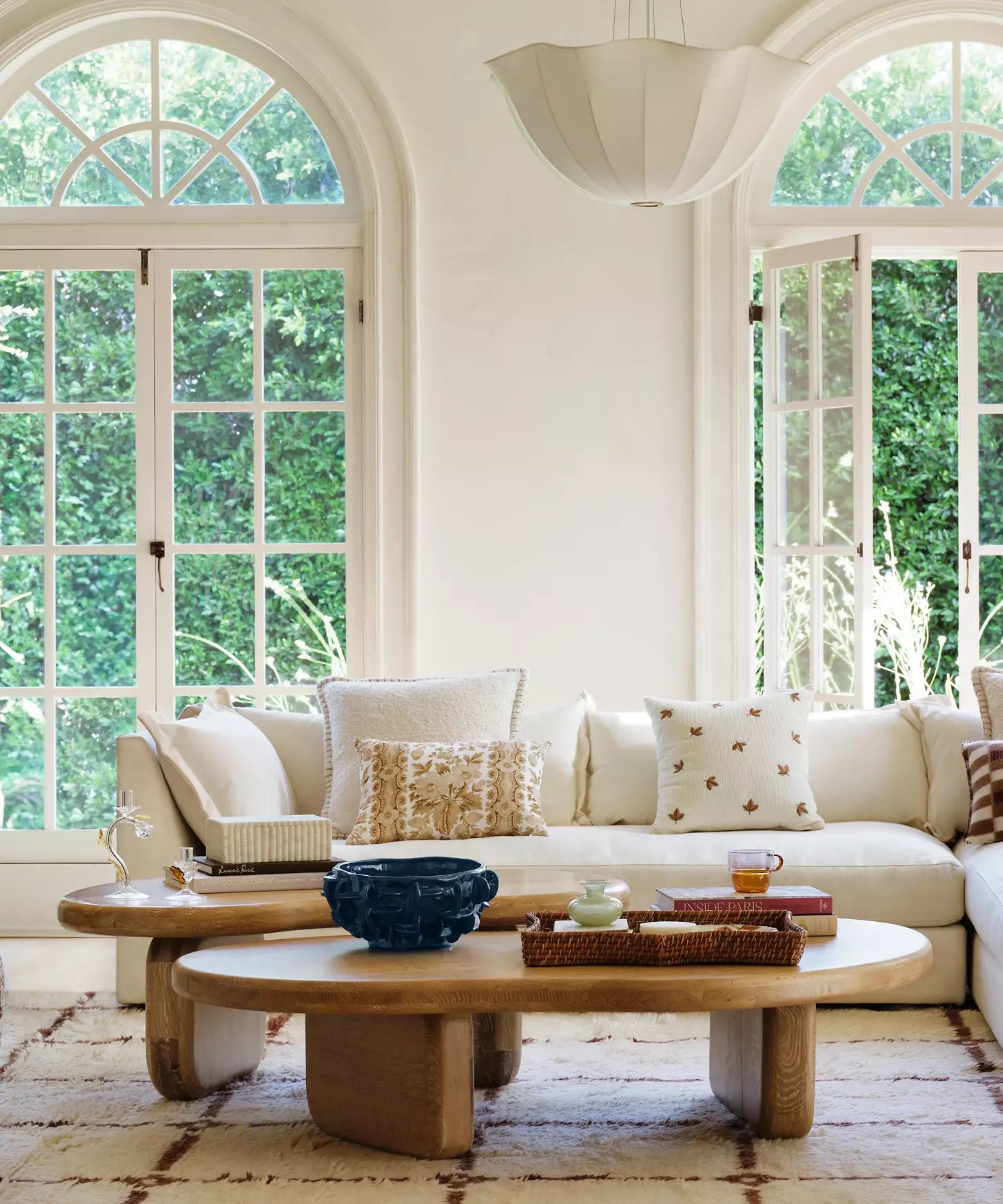 Cream living room with big arched windows, a cream corner sofa with throw pillows and two wooden coffee tables