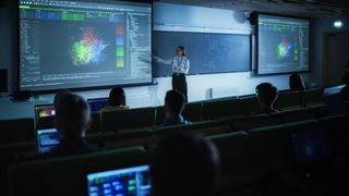 Young University Professor Explaining the Importance of Artificial Intelligence to a Group of Diverse Students in a Dark Auditorium. Female Teacher Showing Big Data Ecosystem on Two Big Screens