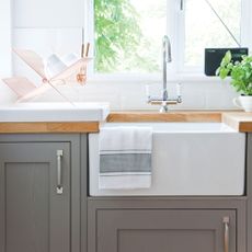 White tiled kitchen with grey cabinets and a white sink with silver taps 
