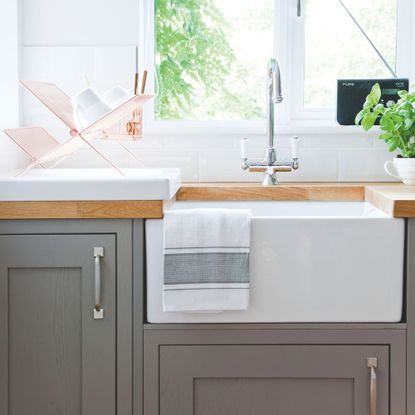 White tiled kitchen with grey cabinets and a white sink with silver taps 