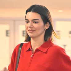 Kendall Jenner wears a red sweatshirt and carries a black leather bag