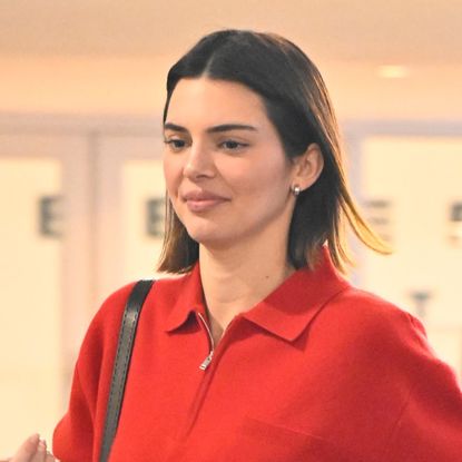 Kendall Jenner wears a red sweatshirt and carries a black leather bag