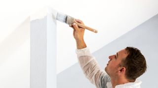 Man cutting in ceiling edge with grey paint on a white ceiling
