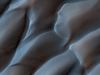 waves of blue sand dunes roll over the surface of mars.