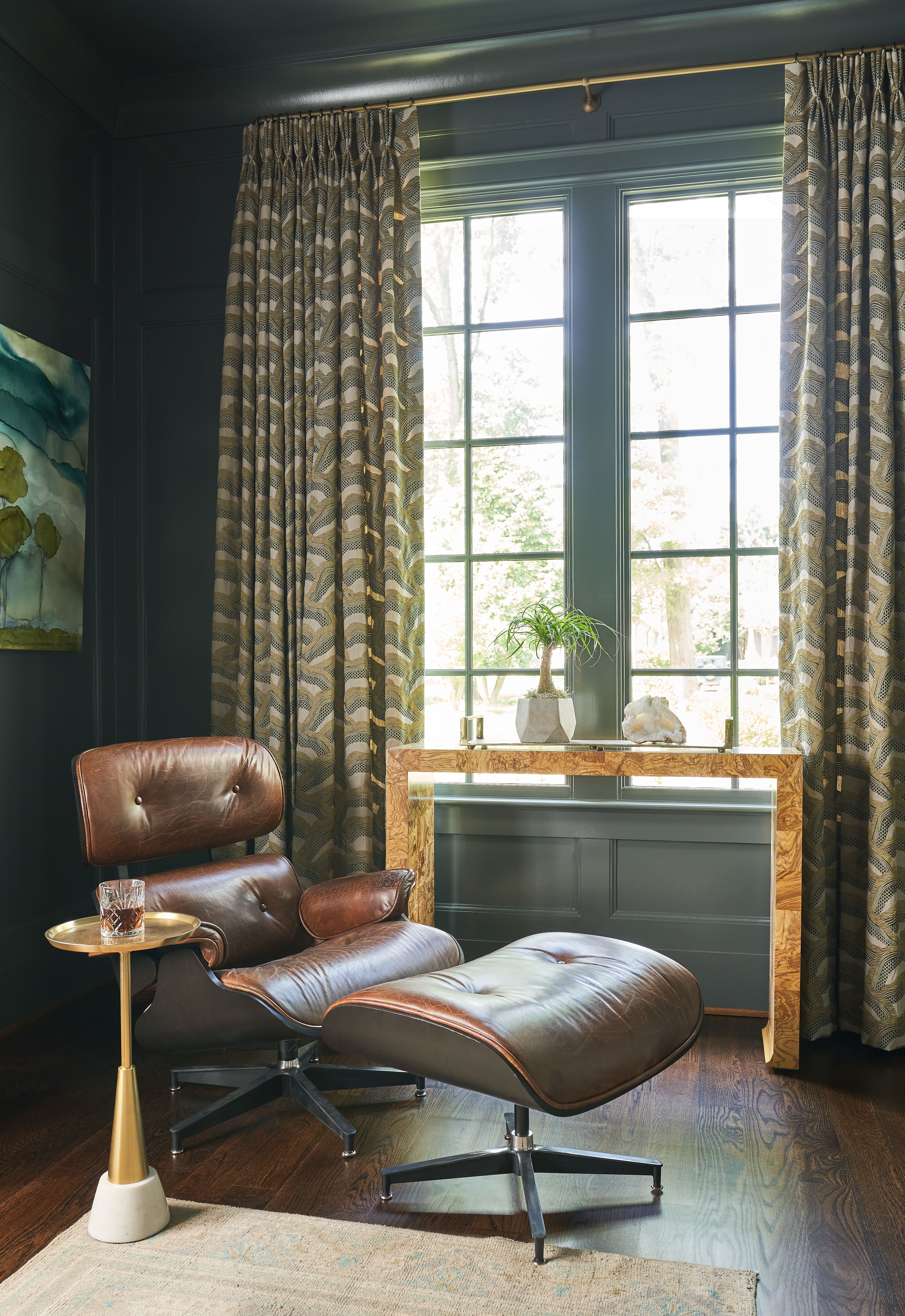 A leather armchair with a footstool to match close by a window with patterned curtains