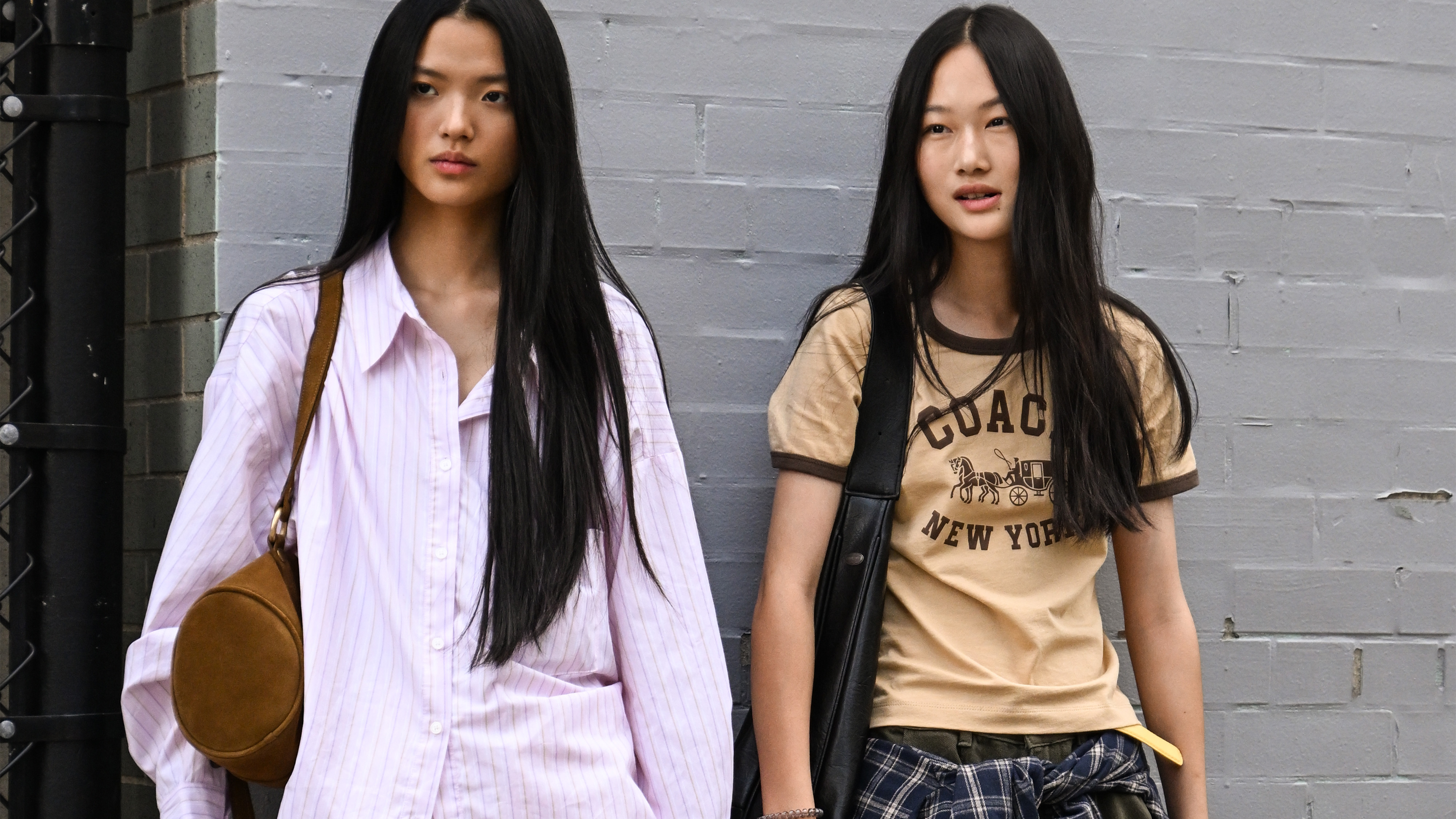 A model is seen wearing a Coach t-shirt, gray pants, plaid shirt and black bag with a model wearing a pink button shirt, white pants and black boots with Coach bag outside the Coach show during womenswear NYFW Spring 2026 on September 15, 2025 in New York City. 