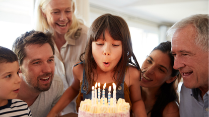 girl blowing out birthday candles surrounded by family