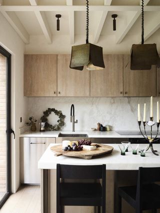 Beige and white kitchen with an island that had candles and a cheese board on it. Square, metal pendant lights hanging above the island