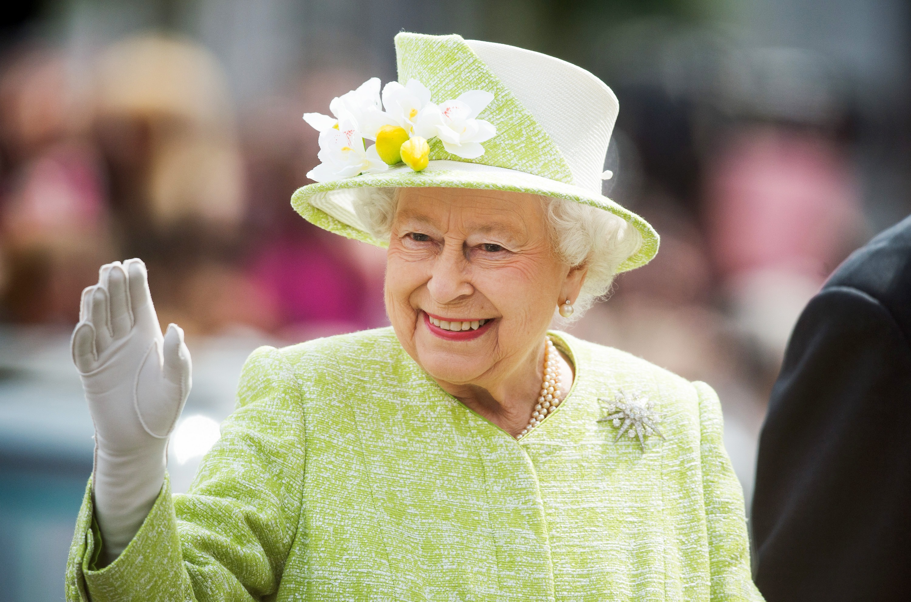 Queen Elizabeth in a light green hat with white flowers and matching coat waving