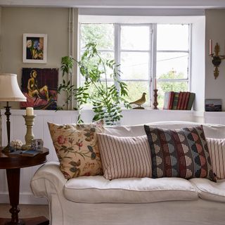 view in old country house living room towards neutral sofa with mixed cushions and window behind