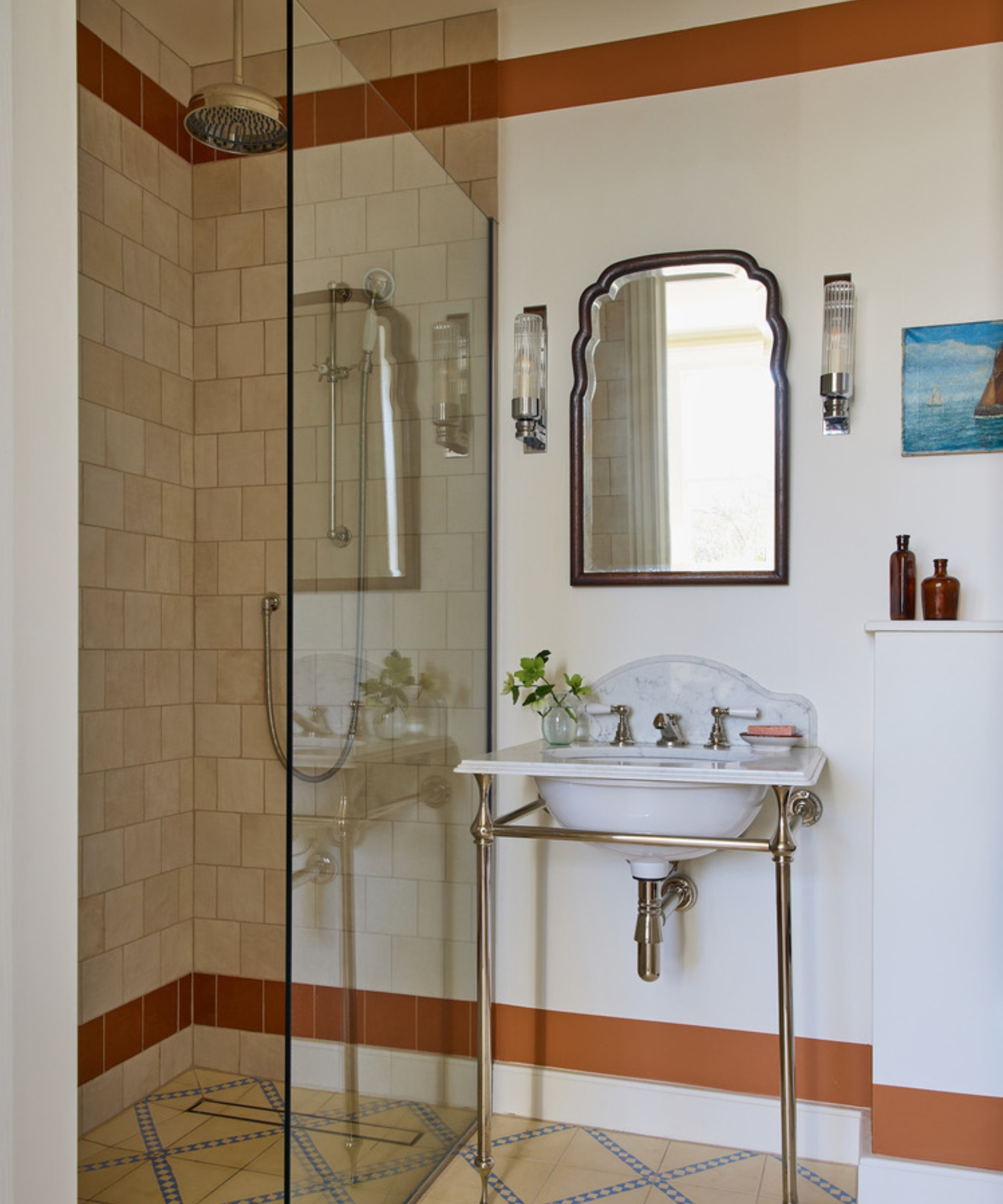 A small shower room with patterned floor tiles and terracotta border tiles at the top and bottom of the walls