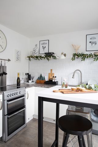 A tall monochrome kitchen table doubles as an island. The walls in the background are tiled with white metro tiles and lined with white units and grey worktops