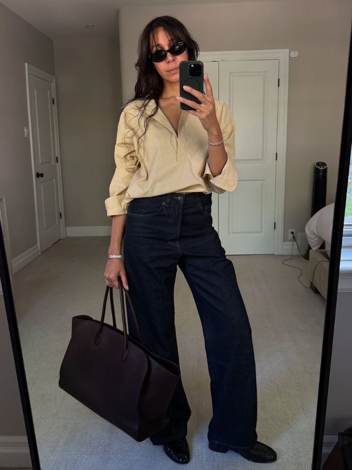 Woman wears yellow shirt, indigo denim jeans and loafers and carries The Row Marlo bag