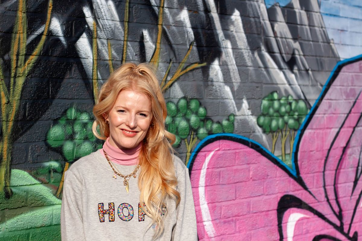 A young woman smiles against backdrop of graffitied wall.