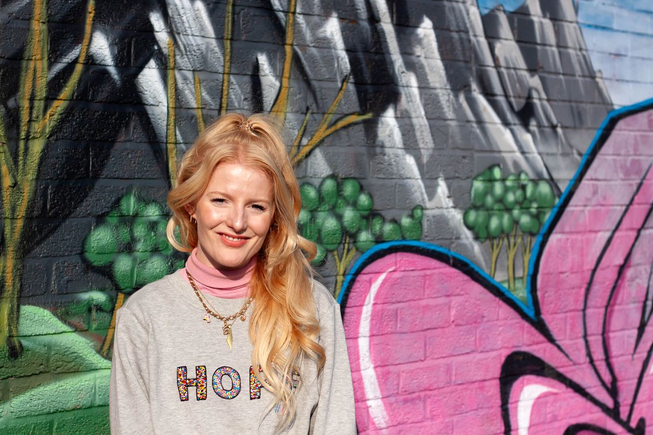 A young woman smiles against backdrop of graffitied wall.