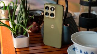 The back of the olive green Motorola Edge 2026 on a tea table next to a potted plant