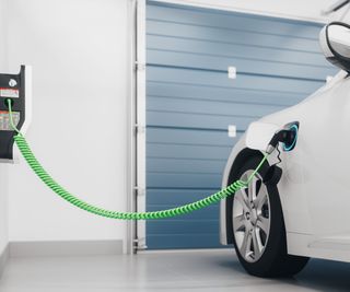 An electric car charging point mounted to a wall at a home in a garage, a green cable charging a white car