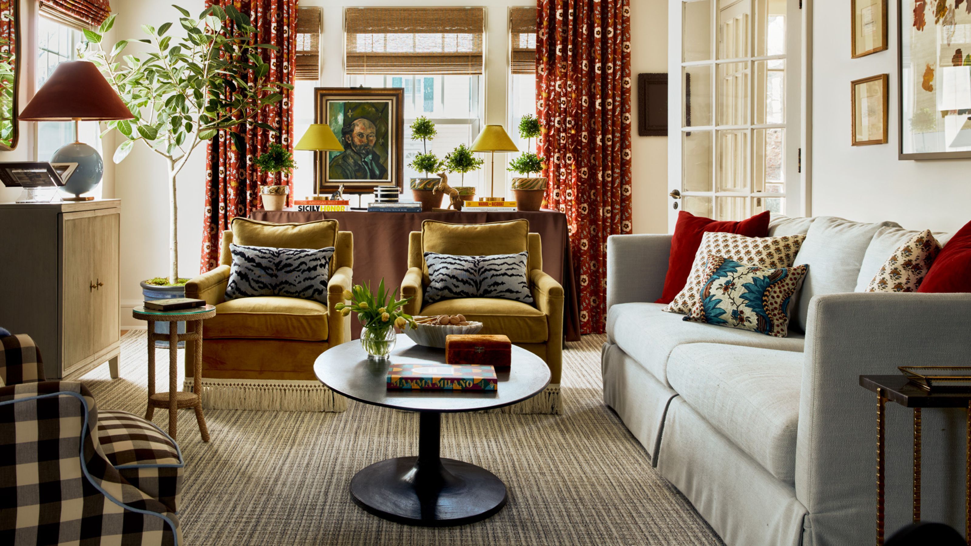 neutral living room with caramel velvet armchairs, a small rounded coffee table, a neutral skirted couch and accents of burgundy