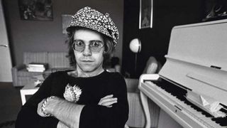 English pop singer Elton John photographed next to his piano at home, mid 1970s.