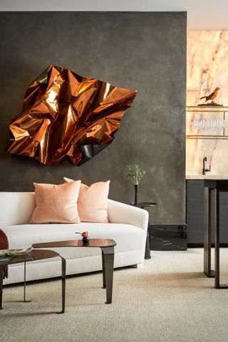 Living area of an open-plan space with textured charcoal walls, black marble skirting, statement copper art piece, white sofa and black coffee table set