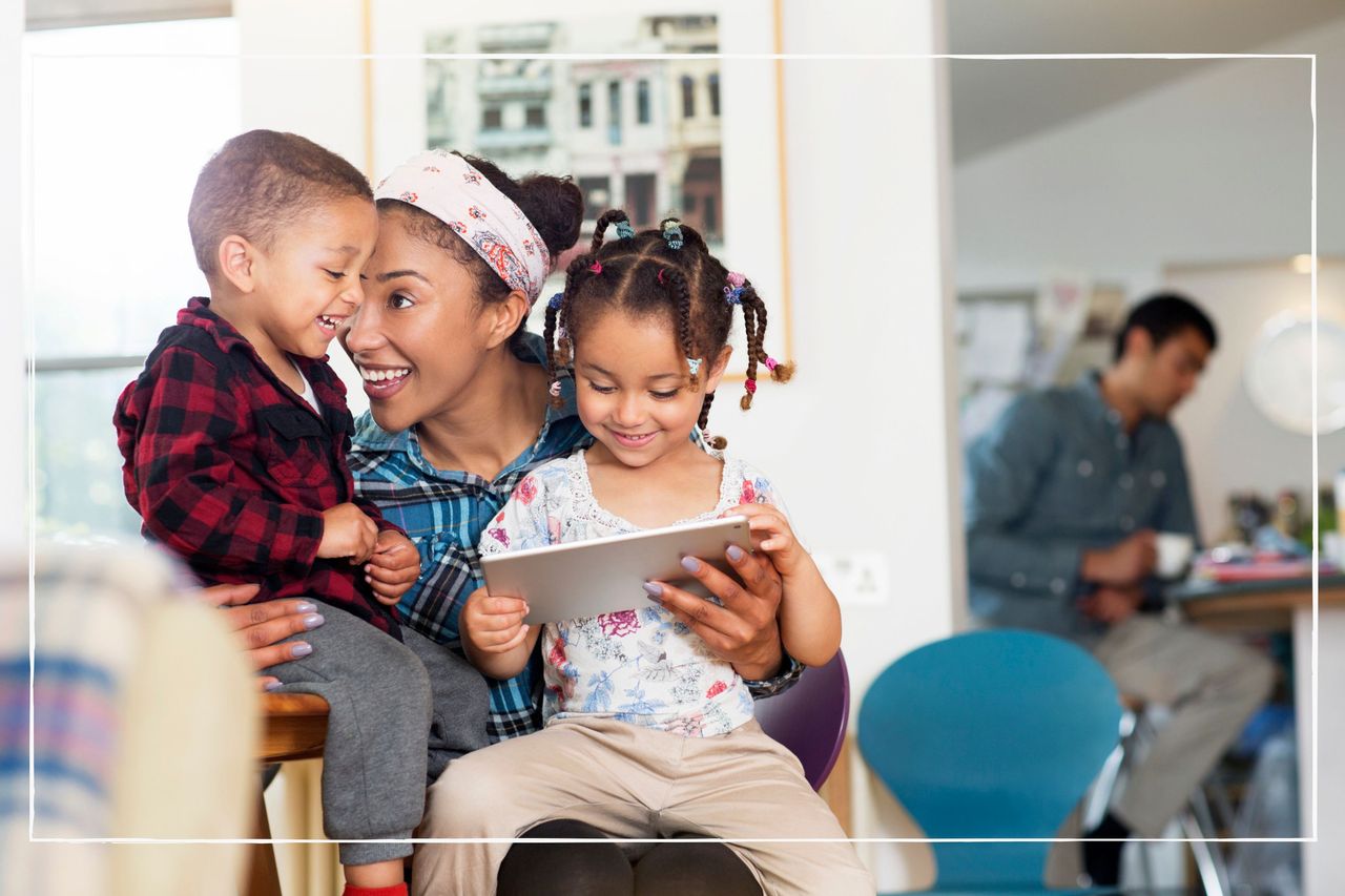 Mother at home looking at iPad with two children on her lap