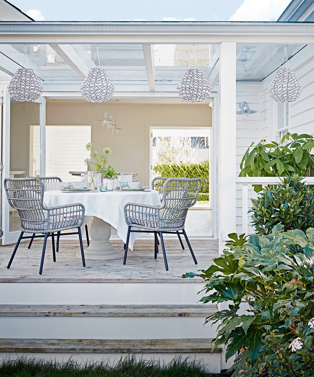 A white outdoor dining area in a garden room with white lanterns and white rattan chairs