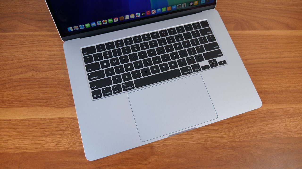 Top down angled photo of the keyboard and touchpad on a silver laptop, on top of a wooden surface.