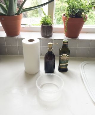 plastic box after tupperware hack, with olive oil, a kitchen towel roll, and plants on the counter too