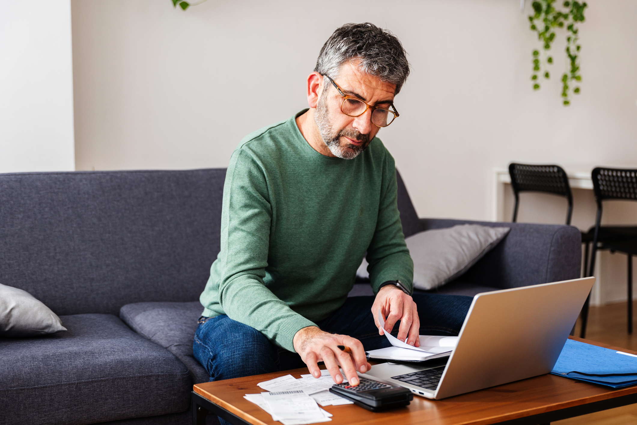 Middle aged man calculating expenses and managing the budget while using a calculator and laptop at home