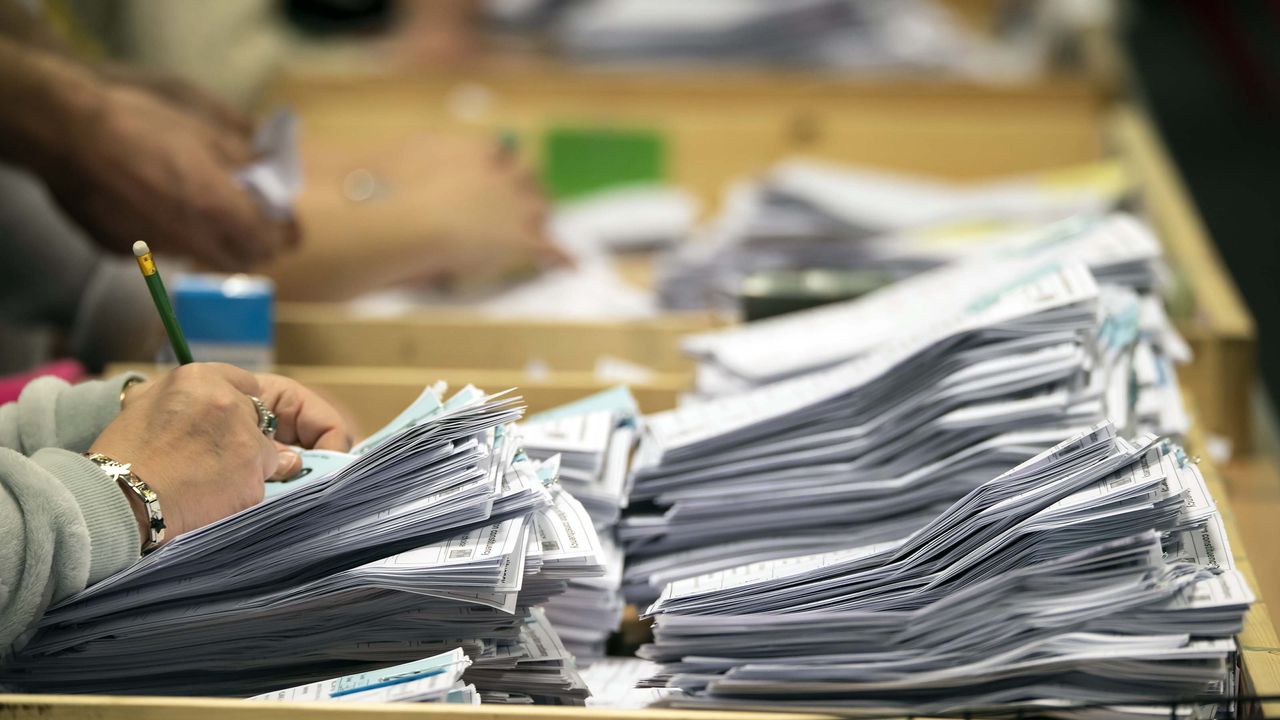 A line of election workers counting ballots at a table.