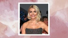 Image of Holly Willoughby smiling with blonde slightly curled bob and wearing a black dimanté strapless dress, on a pink watercolour background