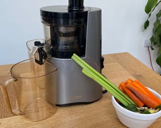 Hurom H-AA slow juicer with a selection of vegetables including celery, carrot, spinach, and ginger