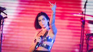 Dua Lipa performing on stage, holding a microphone and flipping the bird