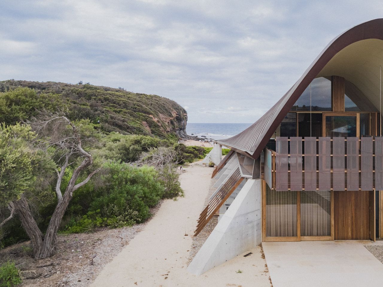 Beach house next to greenery and a cliff with view of the ocean