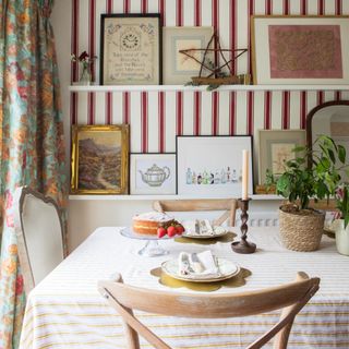 A dining room with a vertically striped wallpaper on the wall and a horizontally striped tablecloth on the dining table