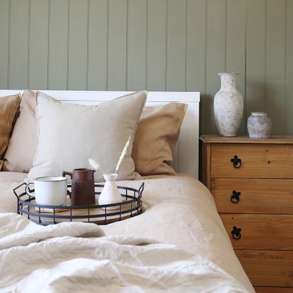 A bed with natural coloured bedding and a green panelled wall behind