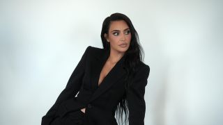 Kim Kardashian in Season 5 of The Kardashians wearing a black suit and leaning to her right against a black background.