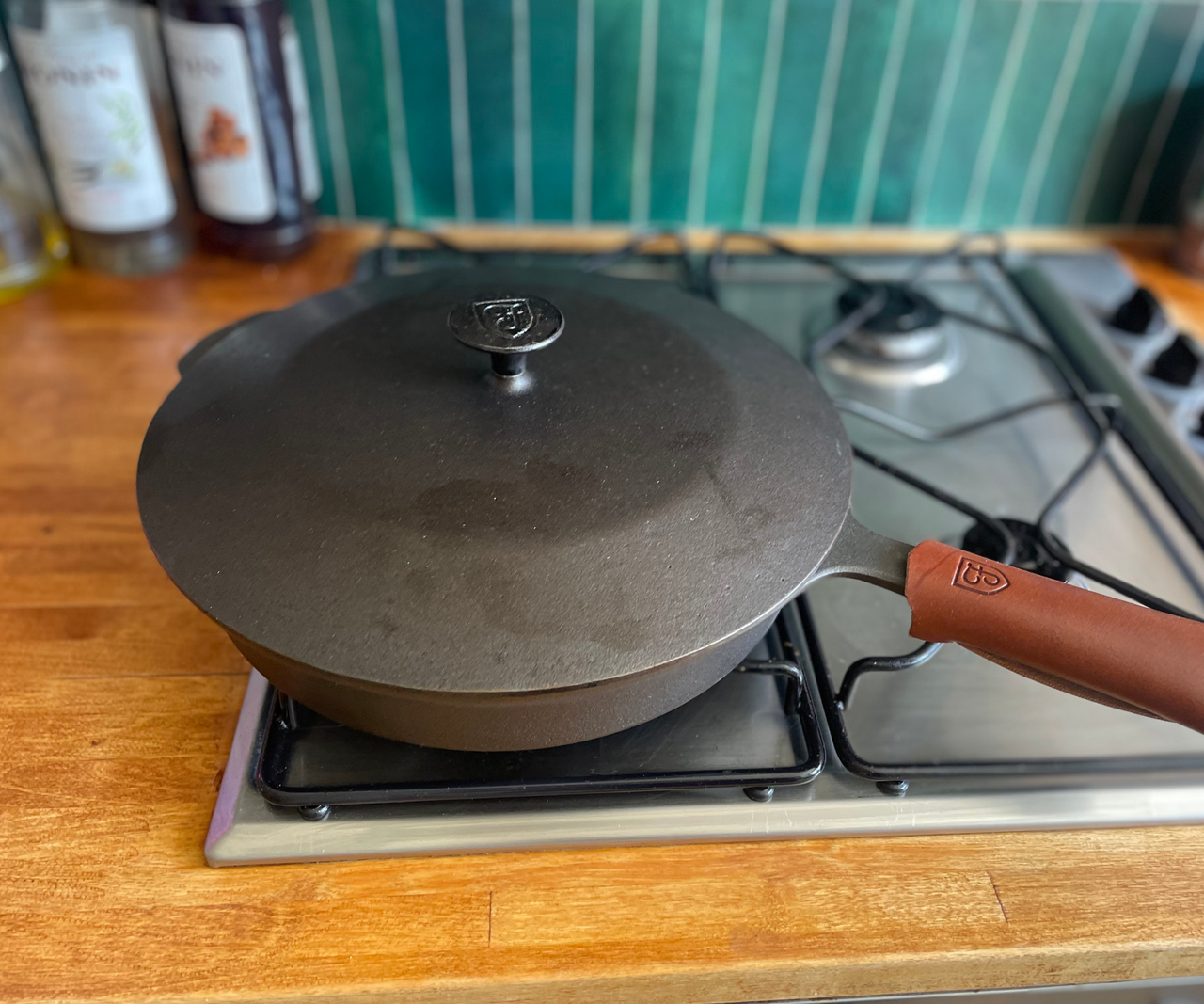 A grey cast iron skillet with a lid on top, on a gas stove range set into wooden counter tops.